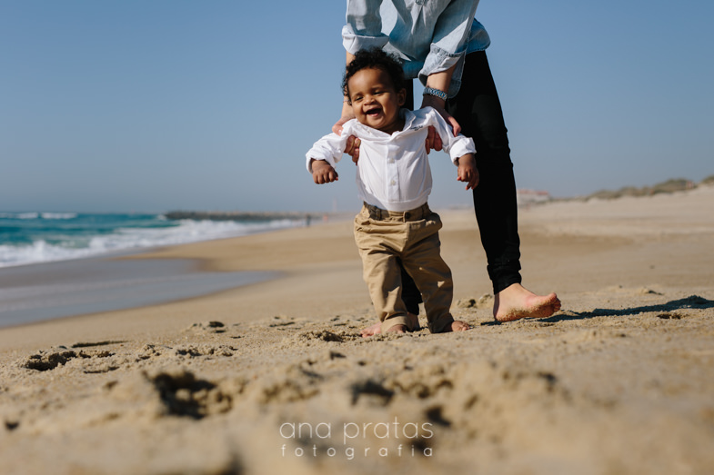 mom holding his son while he attempts to walk on sand